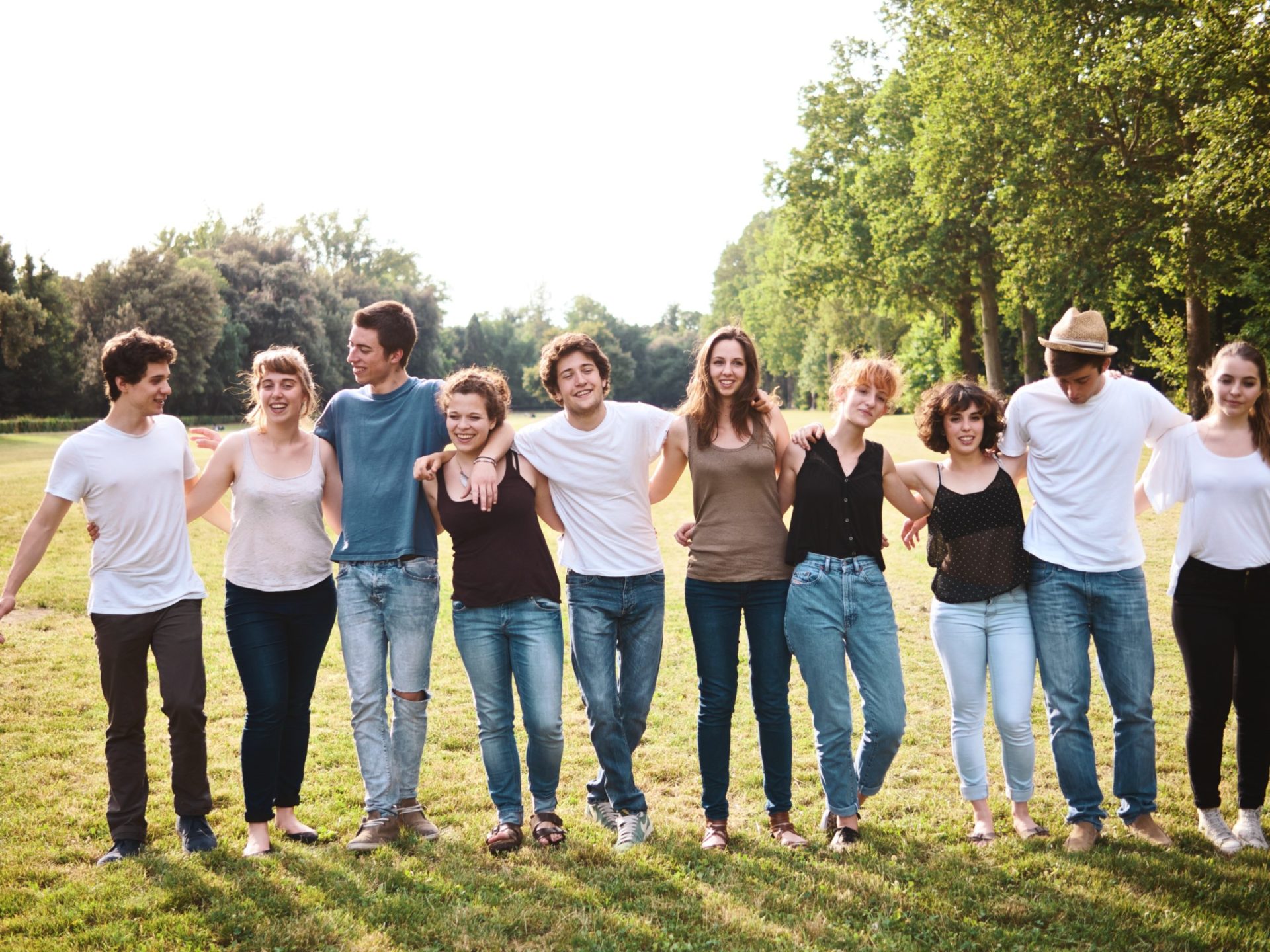 Group of ten young people standing arm-in-arm on grass, smiling together outdoors